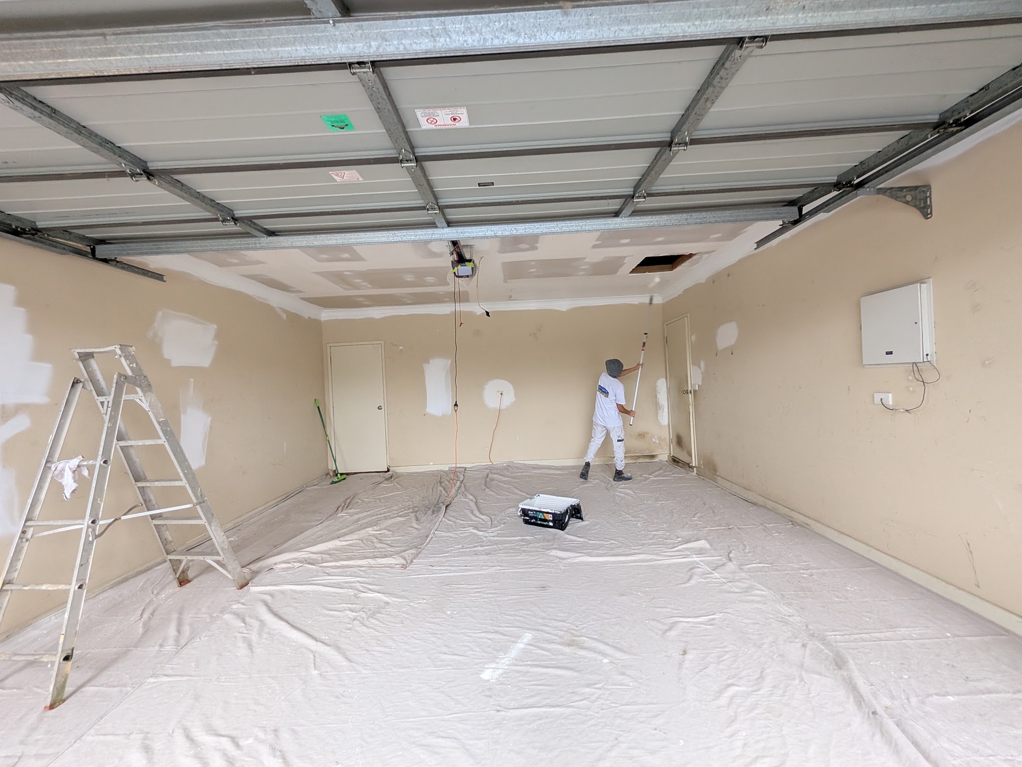 A Roz Coatings and Colours painter rolling a garage ceiling line, drop sheets across the floor