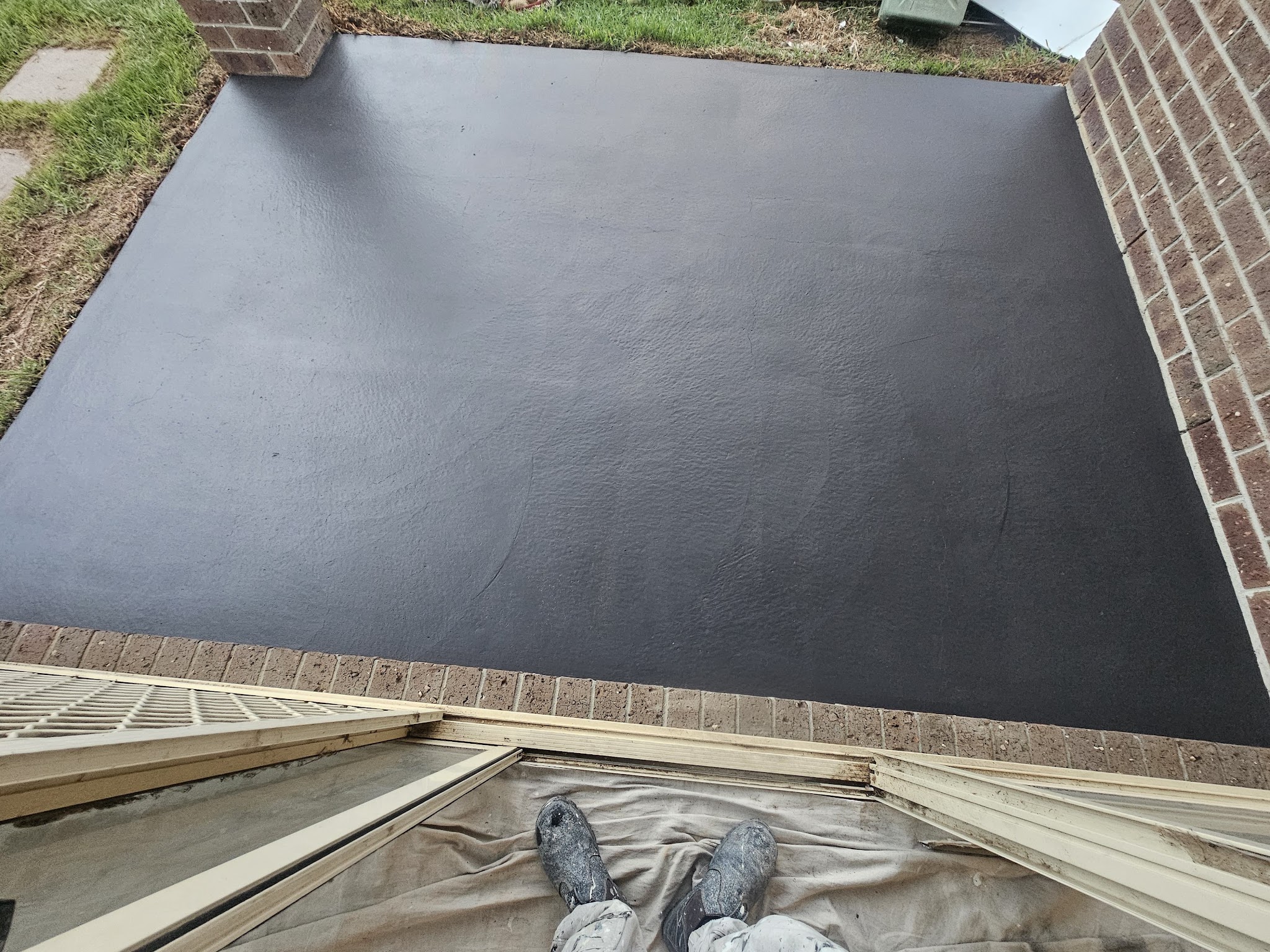 Freshly coated charcoal concrete patio beside a brick house